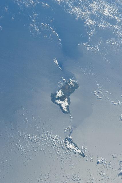 Grande Comore appears in the center of this view with Moheli (mostly cloud covered) toward the bottom. The silvery surface of the Mozambique Channel is due to sun glint. Photo courtesy of NASA.