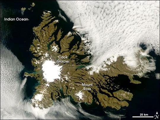 A rare break in the clouds allowed a satellite a chance to capture this photo-like image of the Kerguelen Islands. Located in the southern Indian Ocean roughly midway between Africa, Australia, and Antarctica, the Kerguelen Islands experience a fierce climate, with incessant, howling winds and rain or snow nearly every day. At a latitude of about 49 degrees south, the islands lie in the path of the "Furious Fifties," a belt of westerly winds that whip around the Southern Hemisphere, mostly unimpeded by land.
The islands were formed over millions of years by a series of lava flows. The perimeter of the large island is carved by fjords, and the rocky landscape is very sparsely vegetated with grasses, mosses, and a plant in the cabbage family. Glaciers are scattered across the island. The largest is Cook Glacier, in the west. The highest point on the island is Mount Ross, which has an elevation of 1,850 m; it is also thought to be the youngest volcanic peak on the island. In a handful of fjords, the water appears greenish. The color is probably due to very fine sediment ground down by the enormous friction the glaciers generate as they scrape over the land. Rivers and streams flush this sediment out to the coast.
Despite the challenging climate, several animals and birds make their homes at Kerguelen or use it as a stopping over point in their migrations or during breeding. Among the wildlife on the Kerguelen Islands are several species of penguins, elephant and fur seals, and dozens of species of birds, including terns and albatrosses. The sea makes this "wildlife sanctuary" possible; the islands are located along the Antarctic Convergence Zone, where the icy waters of the Southern Ocean meet the warmer waters of the Indian Ocean. The waters in this mixing area are very rich in nutrients, which support ocean plants (phytoplankton) that are the foundation of the ocean food web. Photo courtesy of NASA.