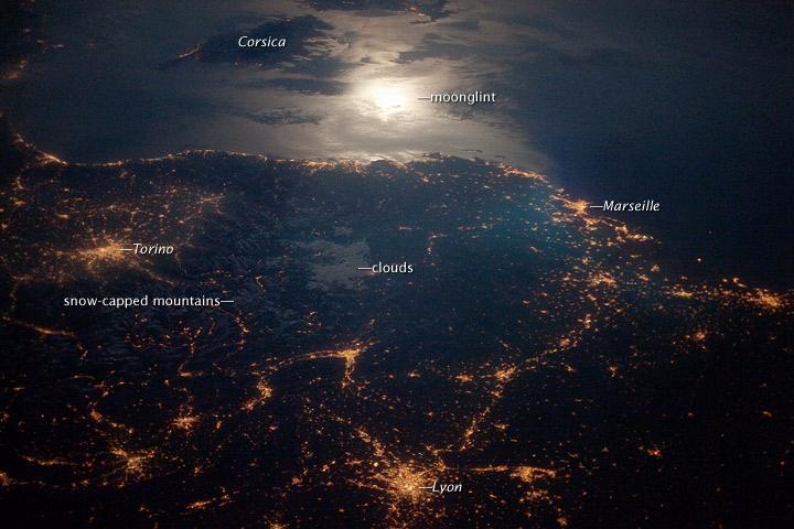 The brightly lit metropolitan areas of Torino (Italy), Lyon, and Marseille (both in France) stand out amidst numerous smaller urban areas in this dramatic photo from the international space station. The image captures the nighttime appearance of the France-Italy border. The southwestern end of the Alps Mountains separates the two countries. The island of Corsica is visible in the Ligurian Sea to the south (image top). The full moon reflects brightly on the water surface and also illuminates the tops of low patchy clouds over the border (center). Image courtesy of NASA.