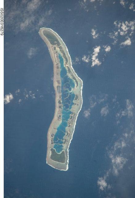 Millennium Island - known as Caroline Island prior to 2000 - is located at the southern end of the Line Islands, which make up the western portion of Kiribati. Uninhabited Millennium Island is formed from a number of smaller islets built on coral reefs. The reefs grew around a now-submerged volcanic peak, leaving a ring of coral around an inner lagoon. The shallow lagoon waters are a lighter blue than the deeper surrounding ocean water; tan linear "fingers" within the lagoon are the tops of corals. The two largest islets are Nake Islet (on the north) and South Islet. Image courtesy of NASA.