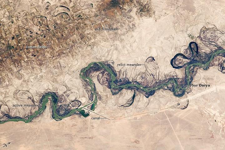 Central Asia's most important cotton-growing region is concentrated in the floodplain of the Syr Darya. The floodplain is shown here as a tangle of twisting meanders and loops (image center). The darkest areas are brushy vegetation along the present course (filled with blue-green water); wisps of vegetation are also visible along flanking swampy depressions, or sloughs. An older floodplain appears as more diffuse dark vegetation (image upper left), where relict bends are overlain by a rectangular pattern of cotton fields. The straight channel of a new diversion canal can be seen along the east bank of the river. Half the river flow is controlled from reservoirs, and half from direct water take-off from canals. In contrast to the intensive agricultural use of water shown here, water control in the mountain valleys upstream is oriented more toward power generation.
The river flows for 2,200 km (1,370 mi), from the Tien Shan Mountains west and northwest to the Aral Sea. Control of the river is vested in the Syr Darya Basin Water Organization, run by nations with territory in the watershed. Some of the organization's main efforts include accurate gauging of water use and repair of canals to reduce widespread water leakage. Photo courtesy of NASA.
