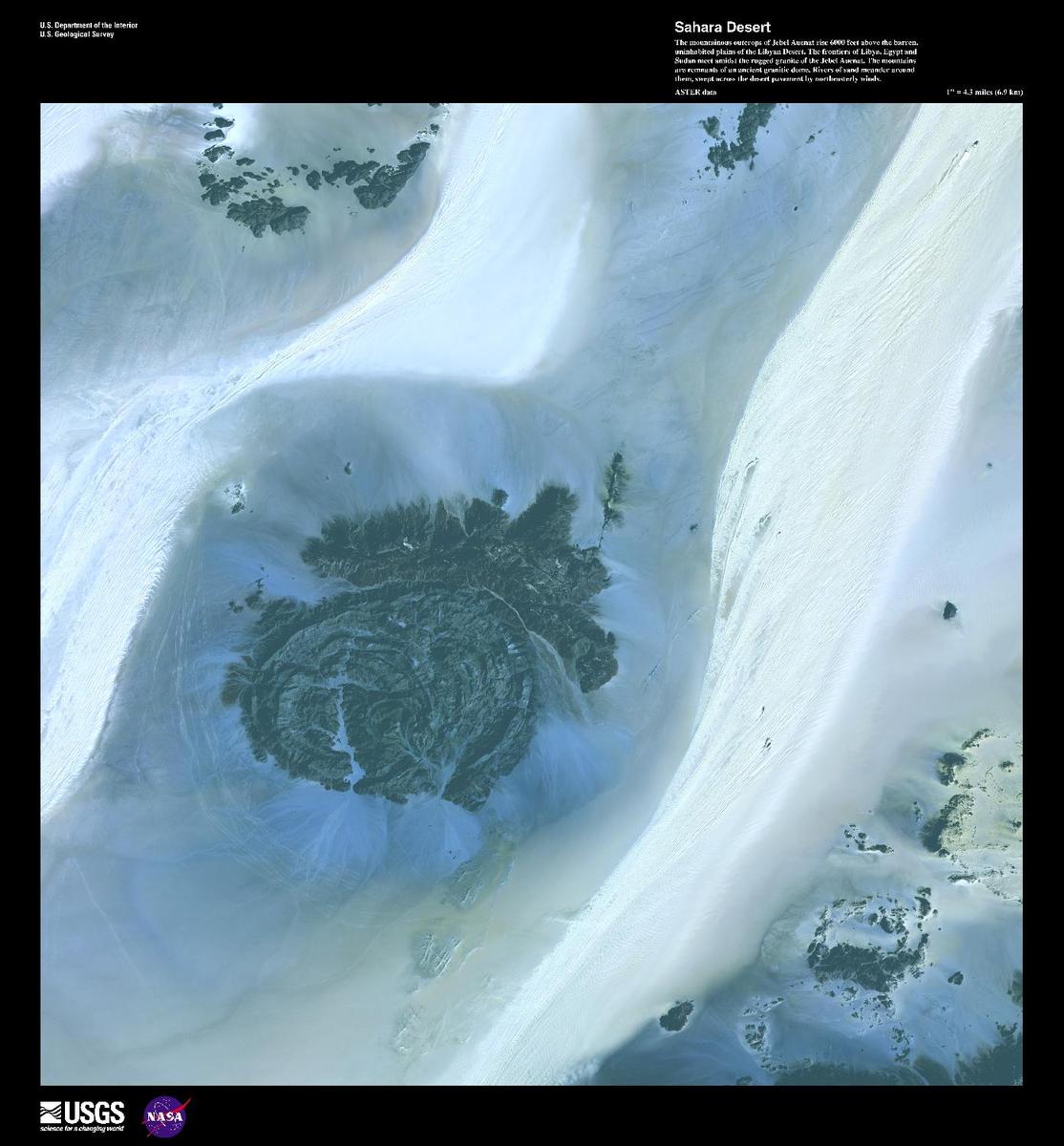 The mountainous outcrops of Jebel Ouenat (Auenat) rise 1,830 m (6,000 ft) above the barren, uninhabited plains of the Libyan Desert. One of the wadis on the western side is the site of a permanent oasis where prehistoric petroglyphs may be found. The frontiers of Libya, Egypt, and Sudan meet amidst the mountains, which are remnants of an ancient granitic dome. Rivers of sand meander around them, swept across the desert pavement by northeasterly winds. False-color satellite image courtesy of USGS.