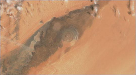 The Richat Structure, a prominent circular feature in the Sahara Desert of Mauritania, has attracted attention since the earliest space missions because it forms a conspicuous bull's-eye in the otherwise rather featureless expanse of the Gres de Chinguetti Plateau in central Mauritania. The Structure, which has a diameter of almost 50 km (30 mi), has become a landmark for space shuttle crews. Initially interpreted as a meteorite impact structure, it is now thought to be merely a symmetrical uplift (circular anticline) laid bare by erosion. Image courtesy of NASA.