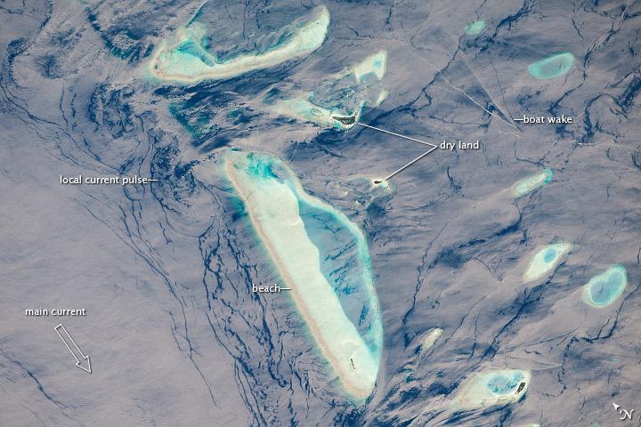 This photograph features one of the numerous atolls in the Maldive Islands chain. The Maldives are an island nation comprised of twenty-six atolls that stretch in a north-south chain for almost 900 km (560 mi) southwest of India. The silvery, almost pink sheen on the normally blue water of the equatorial Indian Ocean in the image is the result of sunglint, which is sunlight reflecting off of water surface directly back towards the observer. The largest island (image center) is 6 km (4 mi) long, and it is part of the 70-km-(40-mi-) long oval-shaped Male Atoll. Shores facing deeper water have well-defined beaches. Numerous small, elliptical coral reef islets are protected within the ring of shallow water to the northeast (image right). These islets are mostly awash at high tide. Image courtesy of NASA.
