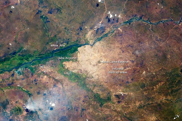 Juba, a port city on the White Nile, is the capital of South Sudan and one of the fastest growing cities in the world. Juba's population is estimated to be roughly 350,000 to 400,000. The city has doubled in size since 2005, when a peace agreement ended the civil war in Sudan. Both hopeful immigrants and returning residents have created the population surge. The city was a central point for humanitarian aid, and the operations base for the UN and NGOs during the Sudanese conflicts. During the fighting, city infrastructure and main transportation arteries suffered heavy damage. The city is still surrounded by army camps and squatter settlements (labeled "informal built-up areas" in the image). They appear as muted gray areas extending outward from the center of the city. The city also hosts the Juba Game Reserve, a protected area of savannah and woodlands that is home to key bird species. Since independence, a variety of countries and international organizations have helped rebuild Juba's roads, railroads, and airport. Unfortunately, South Sudan continues to experience local wars with a variety of armed groups, including on-going conflicts with Sudan over oil-rich territories. Image courtesy of NASA.