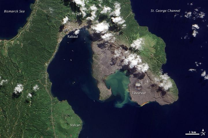 Volcanic cones and settlements mingle along the margins of the Rabaul Caldera on the northeastern tip of Papua New Guinea's New Britain Island. Shaped like a giant cauldron, the caldera is the remaining rim of an ancient volcano. Small volcanic cones, some of which are still active, sit on the rim. Spanning roughly 8 by 14 km (5 by 9 mi), the caldera is flooded by Blanche Bay. The largely submerged caldera long formed a natural harbor for what had been New Britain's largest city, but a major eruption forced the evacuation of Rabaul City in 1994. Although the city ceased to bustle with activity, at least one volcanic cone remained active for years afterward.
The landscape in this satellite image appears as a mixture of vegetated and bare ground. Vegetation almost completely coats the western side of Rabaul Caldera. Volcanic cones line the northeastern margin of the caldera, and around these cones, the land is mostly rocky and barren.
Tavurvur, near the southern end of the exposed caldera rim, was one of the volcanoes to erupt explosively in 1994. The other was Vulcan, on the western side of the caldera. While vegetation has revived on the slopes of Vulcan, rocks predominate at Tavurvur, evidence of more recent eruptive activity.
Remnants of settlements linger along the caldera's northwestern margin and on a promontory near the caldera's center. Prior to the explosive eruption in 1994, the city of Rabaul had been the provincial capital of East New Britain. After the eruption, the capital was moved to the coastal city of Kokopo, some 20 km (12 mi) to the southeast. Photo courtesy of NASA.