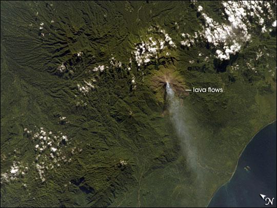 Although Bouganville Island is geographically part of the Solomon Islands chain, politically, the island is part of Papua New Guinea. Bouganville is typical of many Pacific Rim islands in that volcanism has played a large part in both its geological and recorded history. The island hosts three large volcanoes along its northwest-southeast trending axis: Mount Balbi, Mount Bagana, and the Mount Takuan volcanic complex. Mount Bagana, located near image center in this astronaut photograph, is the only historically active volcano on the island.
Within Bouganville's lush landscape, light green vegetation and brown lava flows mark the 1,750-meter-high lava cone of Mount Bagana. The lighter color of vegetation could result from volcanic activity, higher altitude, or both. The eruptive style of the volcano is typically non-explosive, producing thick lobes of lava that run down the flanks and maintain a dome in the summit crater. Occasional pyroclastic flows of rock fragments and volcanic ash have also occurred. This image shows a diffuse white vapor plume extending west-southwest from the summit. Photo courtesy of NASA.