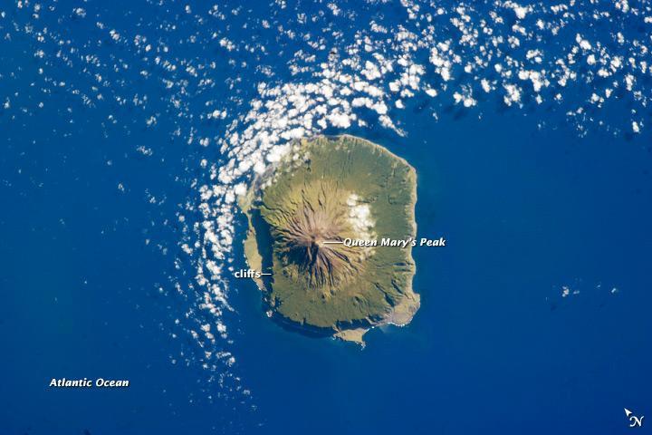 The shoreline of the 13 km (8 mi) wide island of Tristan da Cunha is marked on most sides by steep cliffs, with lower beach areas on the southern and north-northwestern sides. The island is notable for its bird population and includes important breeding grounds for petrels, albatrosses, penguins, and shearwaters.
Tristan da Cunha is a shield volcano, a volcanic structure with a low, broad profile and composed of silica-poor lavas (such as basalt). The upper surface of this low base appears dark green in this astronaut photograph of 6 February 2013. Steeper brown to tan colored slopes mark the central cone of the volcano at the island's center. The summit crater, Queen Mary's Peak, sits at an elevation of 2,060 m (6,760 ft) above sea level. While geologic evidence indicates that eruptions have occurred from the central crater, lavas have also erupted from flank vents along the sides of the volcano and from smaller cinder cones.
The last known eruption of Tristan da Cunha took place in 1961-1962 and forced the evacuation of the only settlement on the island, Edinburgh of the Seven Seas, on the northern coastline (obscured by clouds in this image). The town is considered to be the most remote permanent settlement on Earth, with its nearest neighbor located 2,173 km (1,347 mi) to the northeast on the island of St. Helena. Image courtesy of NASA.