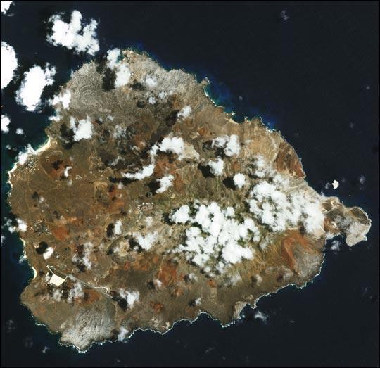 In the southern Atlantic Ocean roughly midway between central South America and central Africa, sits Ascension Island. A small, rocky, volcanic outcrop covered in many places by lava flows and cinder cones of dormant volcanoes, the island sits just west of the Mid-Atlantic Ridge. In this detailed satellite image taken 24 February 2003, marbled-looking lava flows can be seen dominating the northwest coast, with smaller flows visible on the southwest coast below the island's Wideawake Airfield, as well as on the southeast coast. Northeast of the airstrip, a large cinder cone is visible, its dark brown center fading to tan in a series of pale rings. This crater, the island's largest, is called Devil's Riding School. Crisp, white surf breaks along the shores. Image courtesy of NASA.