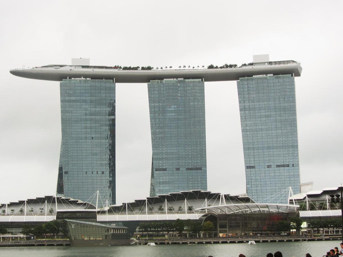 View of the Marina Bay Sands complex in Singapore that opened in 2010 and has since become a city landmark. The three 55-story towers contain hotel rooms. The upper level Sky Park, built to resemble a ship, has the world's longest elevated swimming pool, restaurants, gardens, and a public observation deck. The integrated resort also includes an adjacent ArtScience Museum, a casino, and a convention center.