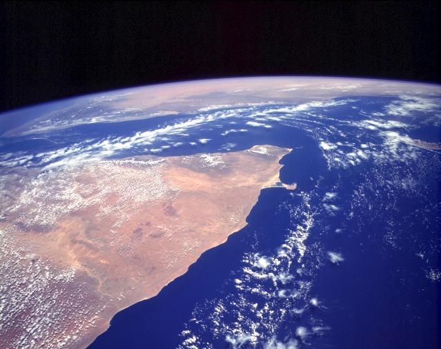 The orange and tan colors of this high-oblique photograph of the Horn of Africa indicate an arid-to-semiarid landscape in the northern half of the east African country of Somalia. Except for the darker areas where thicker vegetation can be found (usually in elevated areas), most of the vegetation in this part of Somalia is shrub brush and grasslands. The southern extent of the Saudi Arabian Peninsula is visible north across the Gulf of Aden. Image courtesy of NASA.
