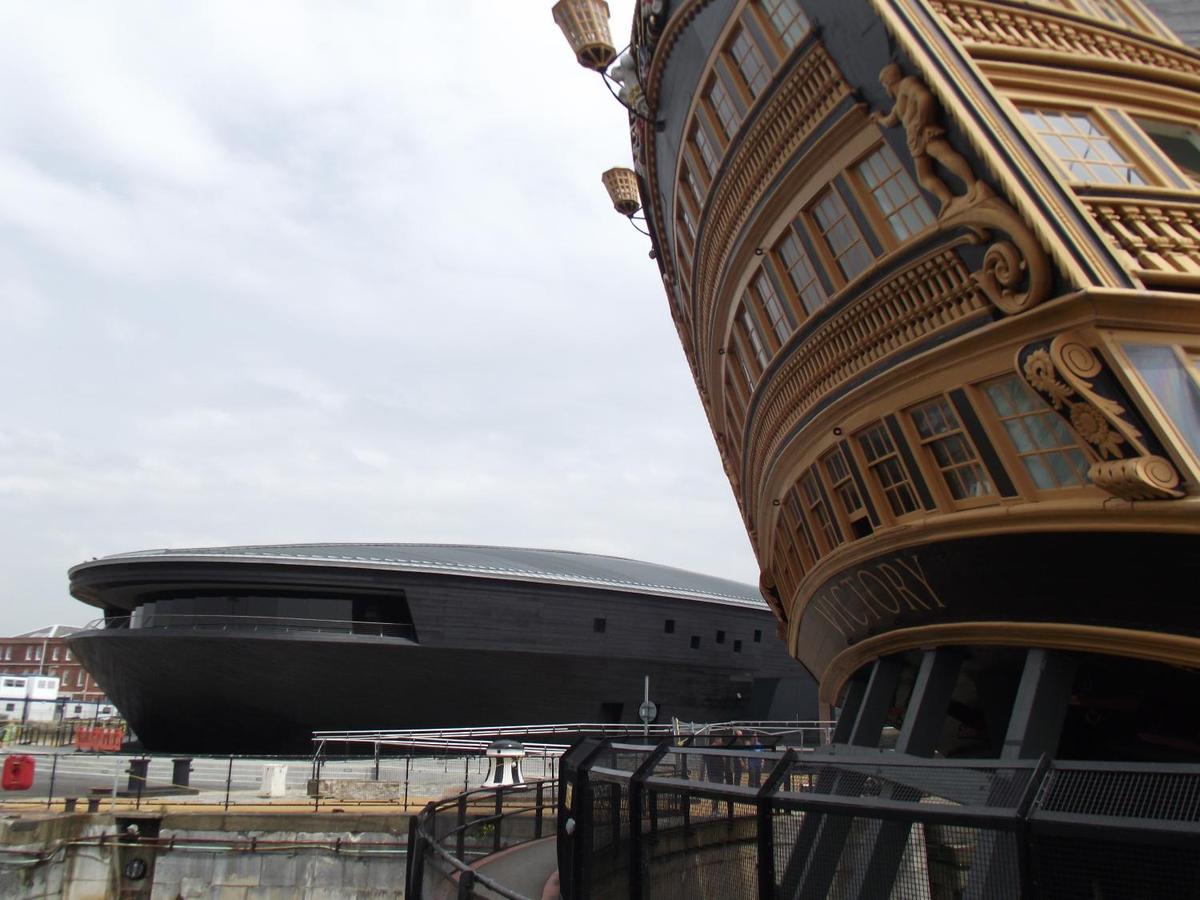 The simple curving lines of the Mary Rose Museum contrast with the ornate carvings on the stern of HMS Victory in the historic dockyard area in Portsmouth, England. The Mary Rose was a 16th-century warship that sank abruptly in 1545 during an engagement with the French. She was salvaged in 1982 along with thousands of artifacts and today serves as the centerpiece of an eponymous nautical museum and maritime archeological center.