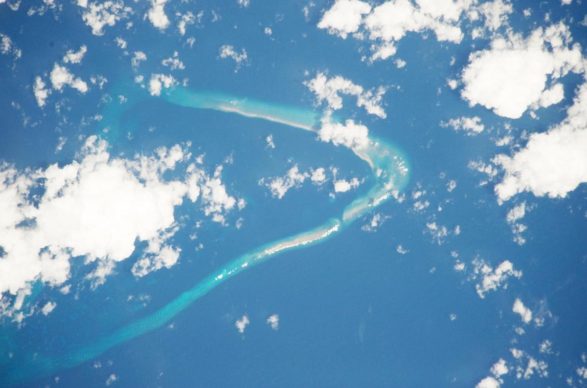 Astronaut photo of Kingman Reef, a largely submerged, uninhabited triangular structure in the North Pacific Ocean, roughly halfway between the Hawaiian Islands and American Samoa. The reef lagoon is 82 m (270 ft) deep at the western part and the total enclosed area is about 76 sq km (29 sq mi). The east-west and northwest-southeast trending small strips of dry land are composed of coral rubble and giant clamshells. The highest point on the reef is less than 1.5 m (5 ft) above sea level, which is awash most of the time, making Kingman Reef a maritime hazard. Image courtesy of NASA.