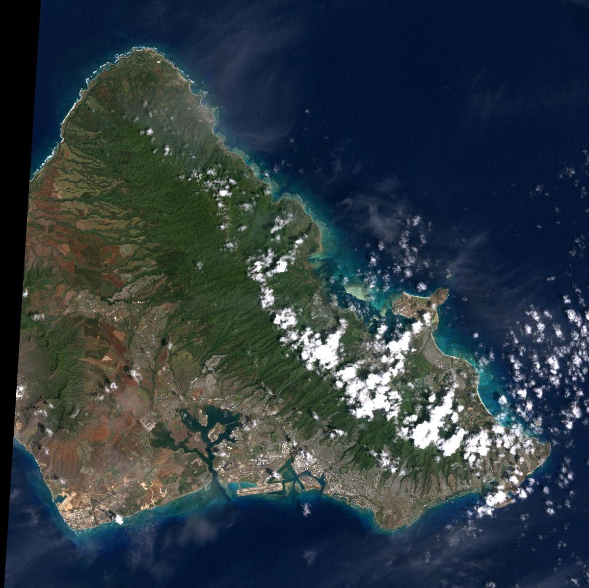 Oahu is the most populated of the Hawaiian Islands. Hawaii's capital of Honolulu stretches along its southern shore. Just to the east of Honolulu is Waikiki Beach, with throngs of tourists and dozens of high-rise hotels. Overlooking Waikiki is Diamond Head, a volcanic crater formed some 200,000 years ago (extinct for about 150,000 years). The clouds in the right hand corner of this image are an almost permanent feature of Oahu. Trade winds blowing from the northeast are stopped by the 960 m (3,000 ft) high mountain range, where they rain out most of their moisture. As a result, the windward side of Oahu is usually cloudy, and the leeward side is relatively clear and dry. The large indent in the lower left of the image is Pearl Harbor, site of the Japanese air raid which drew America into World War II. The harbor still serves as a US Navy base. Photo courtesy of NASA.
