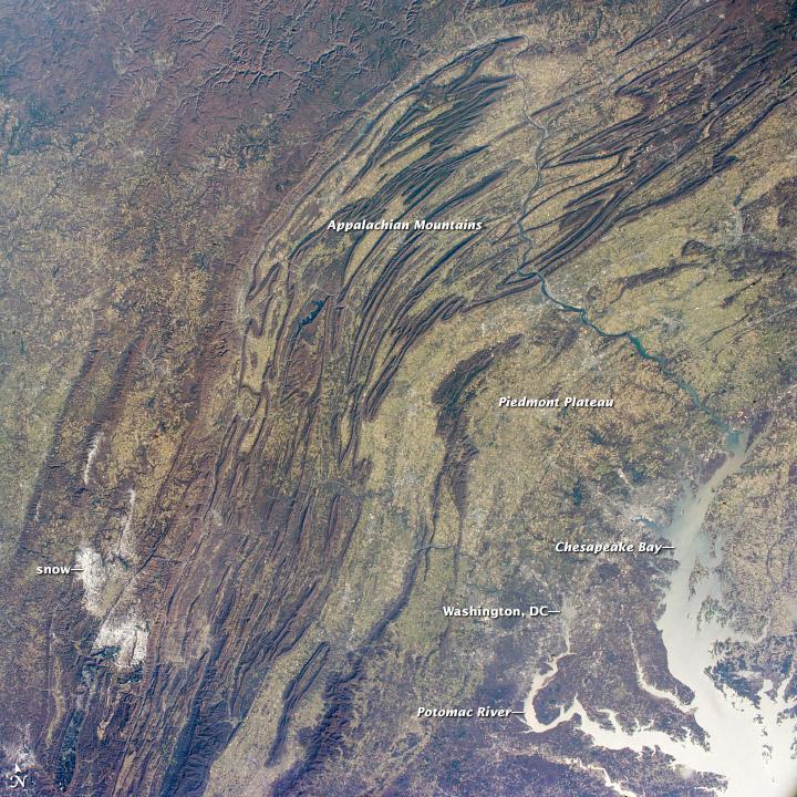This regional view shows the striking visual effect of the valley-and-ridge topography of the Appalachian Mountains as viewed from the International Space Station. The image shows more than 500 km (300 mi) of this low mountain chain from northeast Pennsylvania (top right) to southern West Virginia, where a dusting of snow covers a patch of land (lower left).
Sunglint reflections reveal details of the Chesapeake Bay and the great bend of the Potomac River. Cities are difficult to detect from space during daylight hours, so the sickle-shaped bend of the river is a good visual guide for astronauts trying to photograph the nation's capital, Washington D.C. The farm-dominated Piedmont Plateau is the light-toned area between the mountains and the bay.
The Appalachian Mountains appear striped because the ridges are forested, providing a dense and dark canopy cover, while the valleys are farmed with crops that generally appear as lighter-toned areas. (Farmland is even lighter than usual in this image because the fields are fallow after the harvest.) Photo courtesy of NASA.