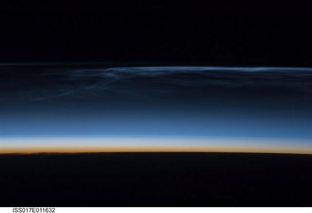 Polar mesospheric clouds (also known as noctilucent clouds) are transient, upper atmospheric phenomena observed usually in the summer months at high latitudes (greater than 50 degrees) of both the Northern and Southern Hemispheres. They are bright and cloudlike in appearance while in deep twilight. They are illuminated by sunlight when the lower layers of the atmosphere are in the darkness of the Earth's shadow. This image was acquired from the International Space Station at an altitude of just over 320 km (200 mi) in the pre-dawn hours. Image courtesy of NASA.