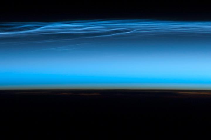 Polar mesospheric clouds - also known as noctilucent or "night shining" clouds - form between 76 to 85 km (47 to 53 mi) above the Earth's surface, near the boundary of the mesosphere and thermosphere, a region known as the mesopause. At these altitudes, water vapor can freeze into clouds of ice crystals. When the sun is below the horizon and the ground is in darkness, these high clouds may still be illuminated, lending them their ethereal, "night shining" qualities.
Polar mesospheric clouds have been observed from all human vantage points in both the Northern and Southern Hemispheres - from the surface, in aircraft, and from spacecraft - and tend to be most visible during the late spring and early summer. Image courtesy of NASA.