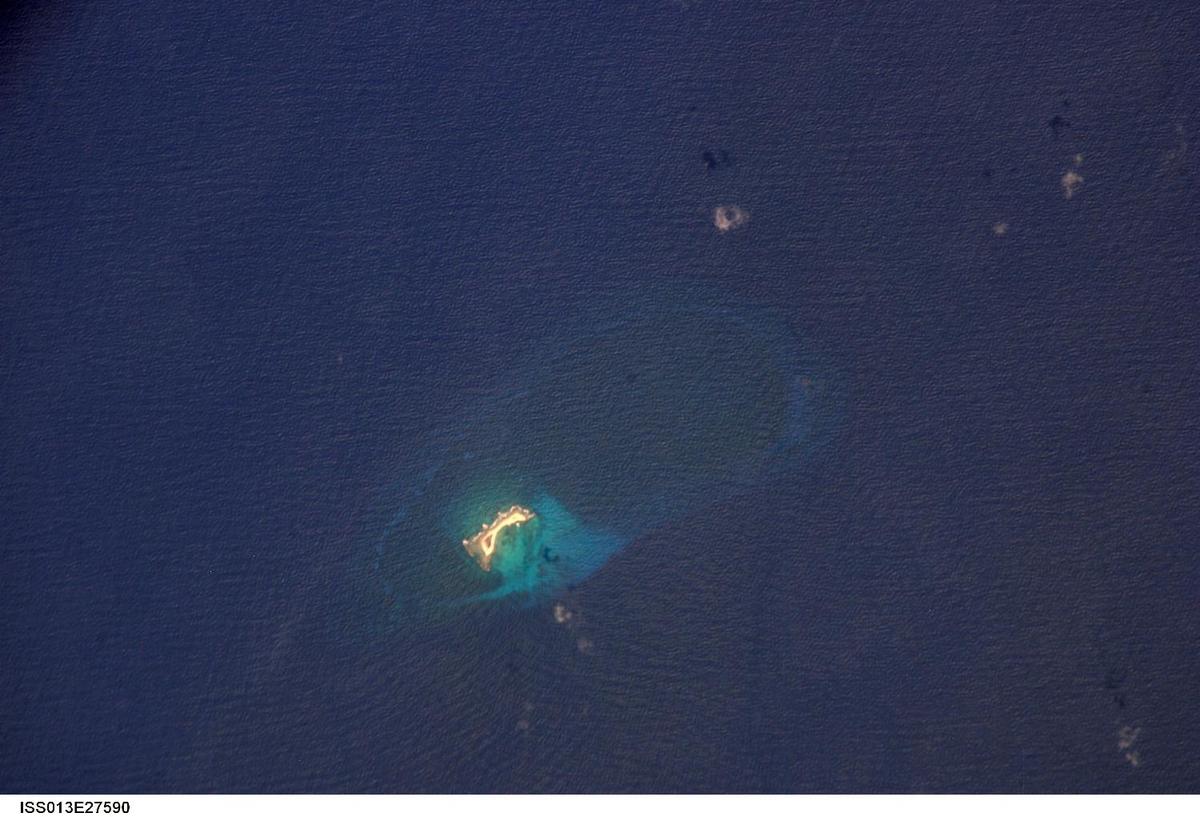 Aves Island in the Caribbean Sea as seen from the International Space Station. This image is a rare, almost cloud free view of the island and the submerged fringing coral reef that surrounds it. The island itself currently stands a mere 4 m (13 ft) above the surrounding sea surface, and in high seas it can be completely submerged. While the low elevation of the island makes it a hazard to shipping, it also provides a major nesting site for green sea turtles. Several Caribbean nations dispute Venezuela's claim to the island. Photo courtesy of NASA.