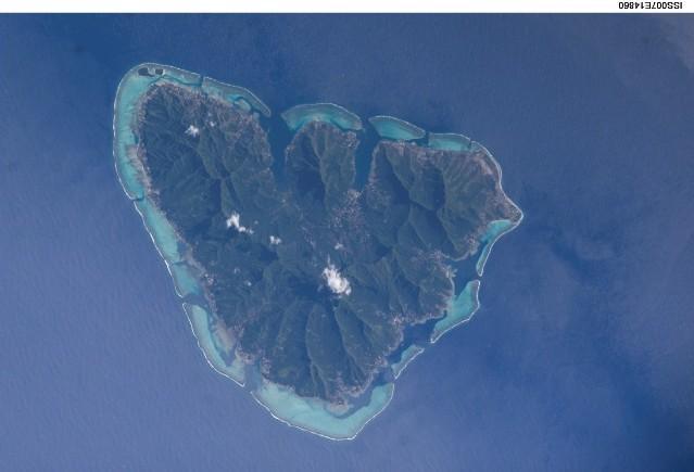 The tropical island of Moorea as viewed from the International Space Station. The barrier reefs surrounding the island create zones of shallow, tranquil light blue waters. Image courtesy of NASA.