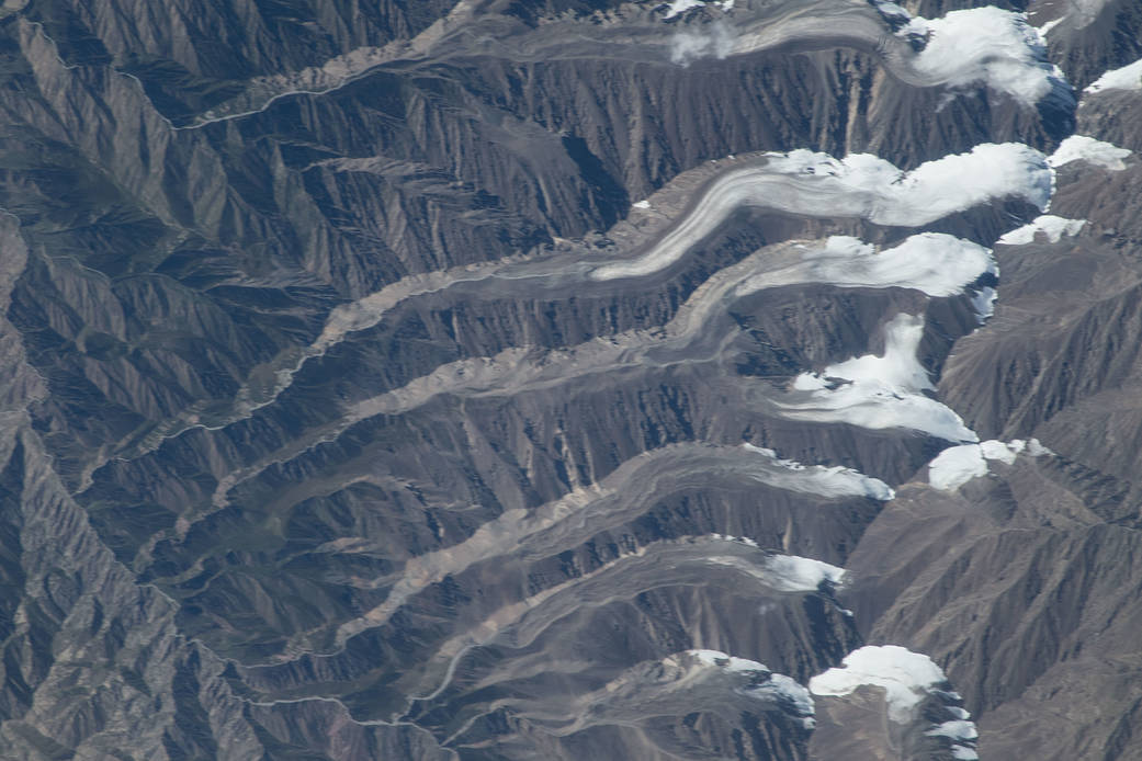 Glaciers in the Qilian Mountain range of central China as viewed from the International Space Station at an altitude of about 400 km (250 mi). The icy tongues extend to the left from the higher elevations at the right. Image courtesy of NASA.