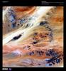 Only 10,000 years ago grasses covered the Sahara Desert and mammals such as lions and elephants roamed the land. Now only two percent of the Sahara hosts oases, patches of land usually centered on natural water springs where crops will grow and where nearly two million people live. In this enhanced satellite image, a series of dark rocky outcroppings contrast with colorful windblown rivers of sand near the Terkezi Oasis in Chad. Image courtesy of USGS.