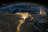 One of the fascinating aspects of viewing Earth at night is how well the lights show the distribution of people. In this view of Egypt, we see a population almost completely concentrated along the Nile Valley, just a small percentage of the country's land area.
The Nile River and its delta look like a brilliant, long-stemmed flower in this astronaut photograph of the southeastern Mediterranean Sea. The Cairo metropolitan area forms a particularly bright base of the flower. The smaller cities and towns within the Nile Delta tend to be hard to see amidst the dense agricultural vegetation during the day. However, these settled areas and the connecting roads between them become clearly visible at night. Likewise, infrastructure and urbanized regions along the Nile River also become apparent.
Another brightly lit region is visible along the eastern coastline of the Mediterranean, the Tel-Aviv metropolitan area in Israel (image right). To the east of Tel-Aviv lies Amman, Jordan. The two major water bodies that define the western and eastern coastlines of the Sinai Peninsula, the Gulf of Suez and the Gulf of Aqaba, are outlined by lights along their coastlines (image lower right). The city lights of Paphos, Limassol, Larnaca, and Nicosia are visible on the island of Cyprus (image top).
Scattered blue-grey clouds cover the Mediterranean Sea and the Sinai, while much of northeastern Africa is cloud-free. The thin yellow-brown band tracing the Earth's curvature at image top is airglow, a faint band of light emission that results from the interaction of atmospheric atoms and molecules with solar radiation at approximately 100 km (60 mi) altitude. Photo courtesy of NASA.