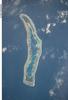 Millennium Island - known as Caroline Island prior to 2000 - is located at the southern end of the Line Islands, which make up the western portion of Kiribati. Uninhabited Millennium Island is formed from a number of smaller islets built on coral reefs. The reefs grew around a now-submerged volcanic peak, leaving a ring of coral around an inner lagoon. The shallow lagoon waters are a lighter blue than the deeper surrounding ocean water; tan linear "fingers" within the lagoon are the tops of corals. The two largest islets are Nake Islet (on the north) and South Islet. Image courtesy of NASA.