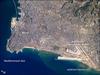 Beirut, Lebanon's capital, is built on a small peninsula; the growth of the city eastwards is bounded by foothills of the more mountainous interior of Lebanon (upper right). Beirut has been an urban center for 5,000 years. Throughout much of that time, the city has been the focus of both military and economic conflicts among neighboring city-states. Distinctive features visible in this astronaut photograph include the Rafic Hariri International Airport in the lower right, the city sports arena at image center, and several areas of green and open space, including a large golf course at image center. Also visible in the photo are several plumes of sediment along the coastline; the most striking plumes are near the airport. The general lack of vegetation in the airport may allow more soil transport by surface water runoff or wind. Photo courtesy of NASA.